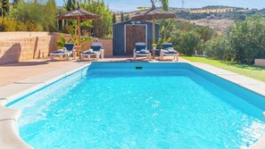 Ein Swimmingpool mit Liegestühlen und einer kleinen Gartenhütte, umgeben von Grünflächen und Hügeln.