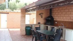 An outdoor kitchen with a grill, a dining table with chairs, a trash bin, and a sink. - Casa Rural de Piedra Valle de Abdalajís by Ruralidays (Málaga)