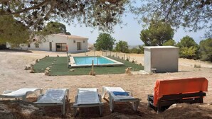 A pool area with lounge chairs and a small building, surrounded by trees.