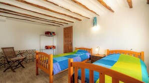 A room with two wooden beds, a chair, a shelf with folded blankets, and a wooden door.