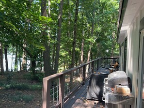 A deck with a grill and outdoor seating area, surrounded by trees. - Adorable 3-bedroom experience on Lake Hartwell with great access to nature (Lavonia)