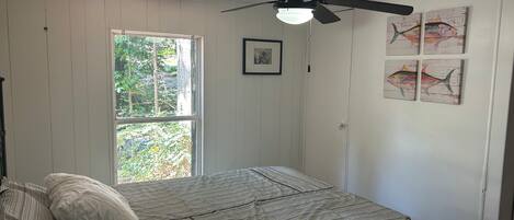 A bedroom with a bed, a ceiling fan, a window, and wall art.