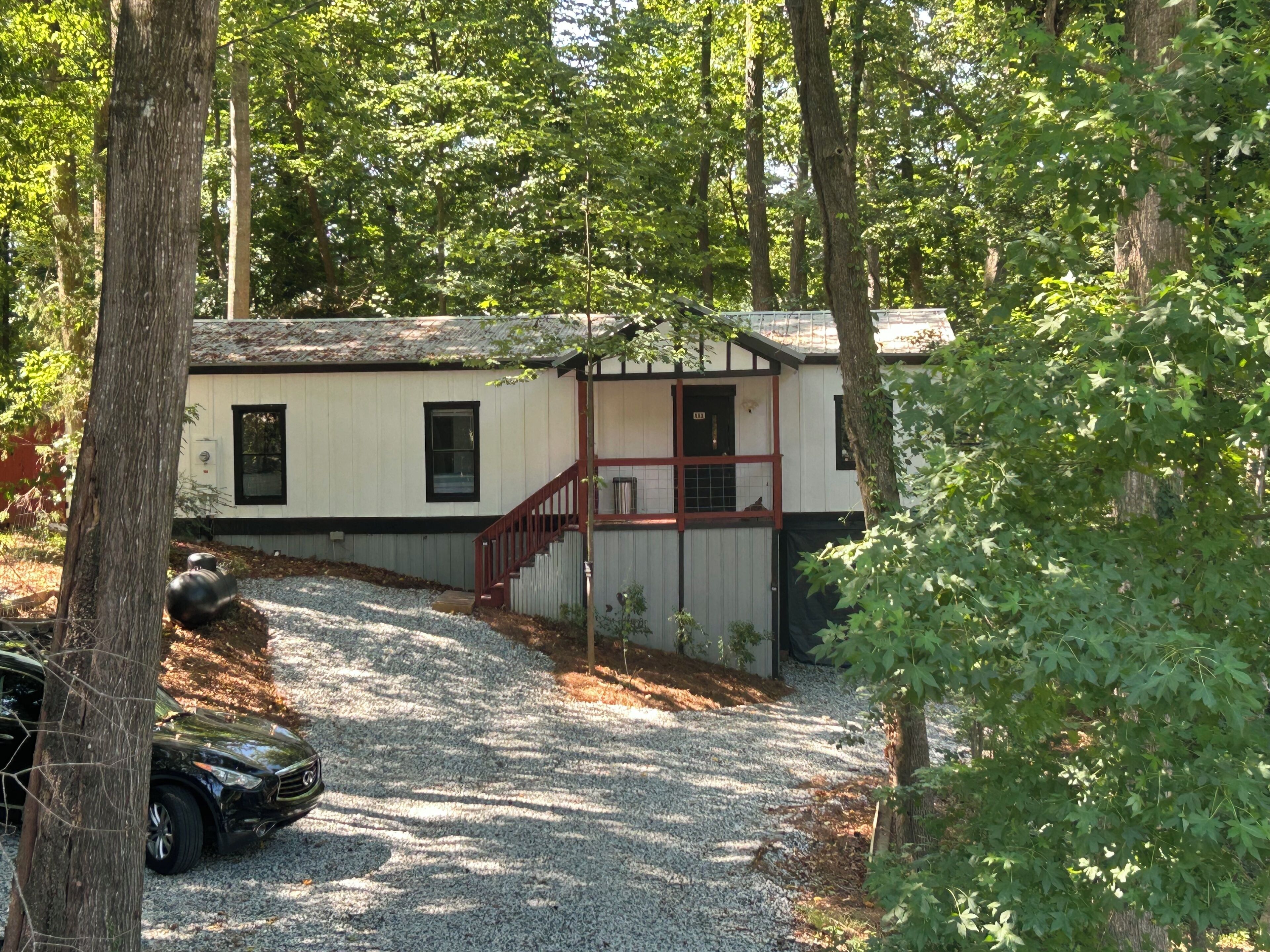 A cabin with a gravel driveway, a staircase, and a car parked nearby.