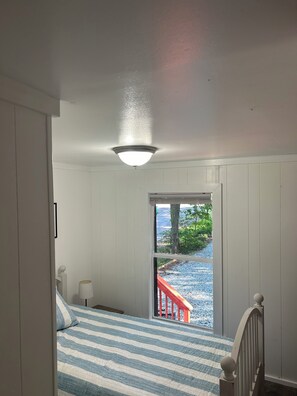 A bedroom with a bed, a nightstand, a lamp, and a view of a red staircase leading outside. - Adorable 3-bedroom experience on Lake Hartwell with great access to nature (Lavonia)