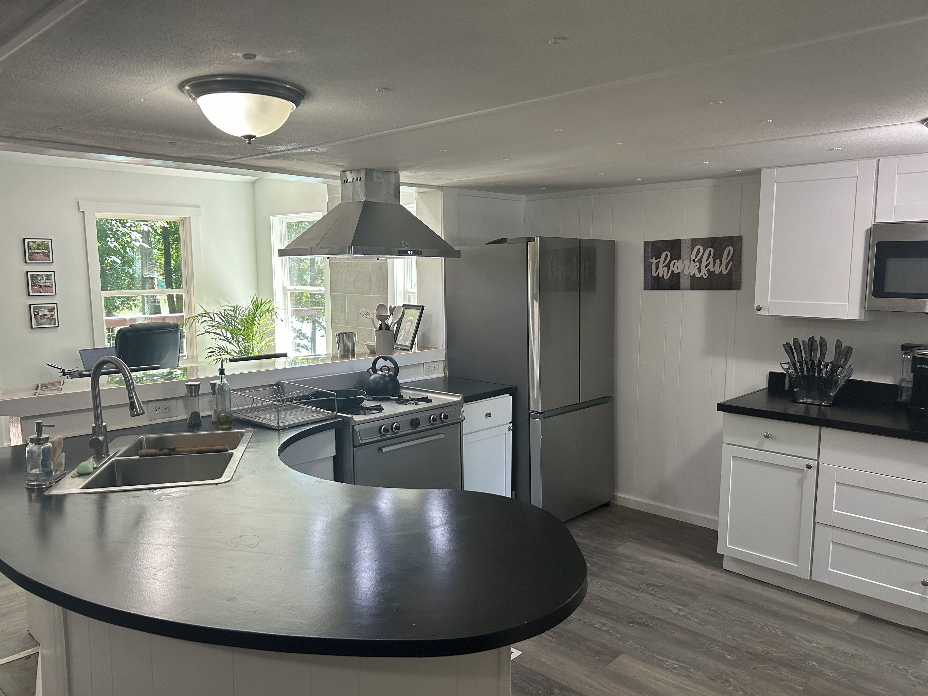 A modern kitchen with a curved island, stainless steel appliances, and a view of greenery outside.