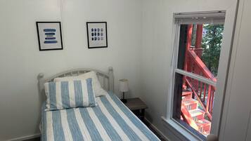 A bedroom with a bed, a nightstand, a window with a view of a red staircase, and two framed pictures on the wall.