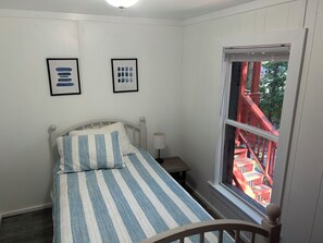 A bedroom with a bed, a nightstand, a window with a view of a red staircase, and two framed pictures on the wall. - Adorable 3-bedroom experience on Lake Hartwell with great access to nature (Lavonia)