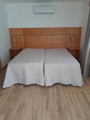 Ein Doppelbett mit Holz Kopfteil, zwei Nachttische mit Lampen und ein Lichtschalter an der Wand.