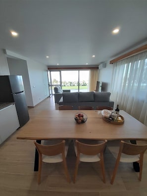 A modern kitchen with a dining area, large windows, and a view of a garden.