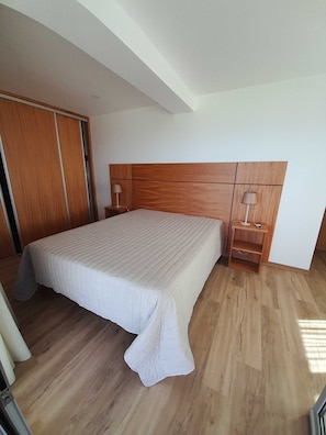 A bedroom with a large bed, wooden headboard, two bedside tables with lamps, and a wooden wardrobe.