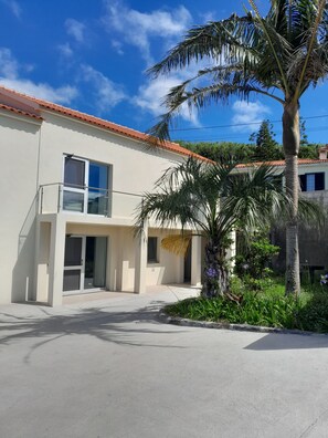 A modern two-story building with a balcony, a palm tree, and a garden.