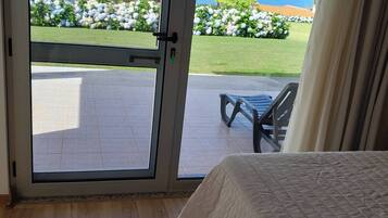 A room with a bed, a sliding glass door leading to an outdoor area with a view of the ocean and a patio with a table and chairs.
