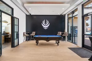 A pool table in a room with a black wall and a logo, two chairs, and a door leading to another room. - ATV Parking + Private spa + Waterpark Hurricane UT (Hurricane)