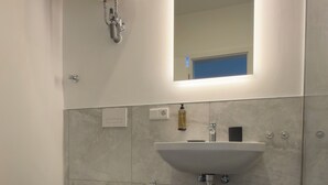 Un baño con inodoro, lavamanos, espejo y cubo de basura.