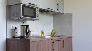Una cocina moderna con microondas integrado, hervidor y un lavamanos pequeño.