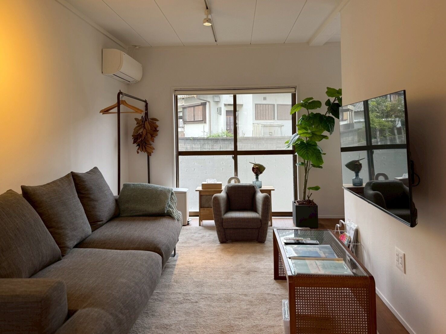 A living room with a sofa, armchair, coffee table, and a large window with a view of buildings.