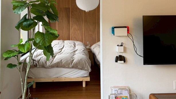 A bedroom with a bed, a potted plant, a wall-mounted TV, and a charging station.