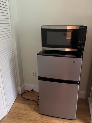 A compact refrigerator with a microwave on top, located in a corner of a room with a wooden floor and a white door. - Cozy 1-bedroom condo in charming Naples six miles from downtown (Naples)