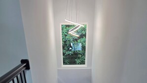 Eine Holztreppe mit schwarzer Geländer, die zu einer Zwischenebene mit einem Fenster mit Blick auf Grünanlagen führt.