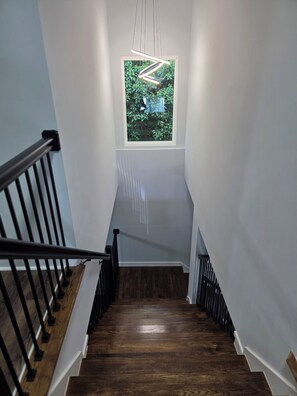 Eine Holztreppe mit schwarzer Geländer, die zu einer Zwischenebene mit einem Fenster mit Blick auf Grünanlagen führt.