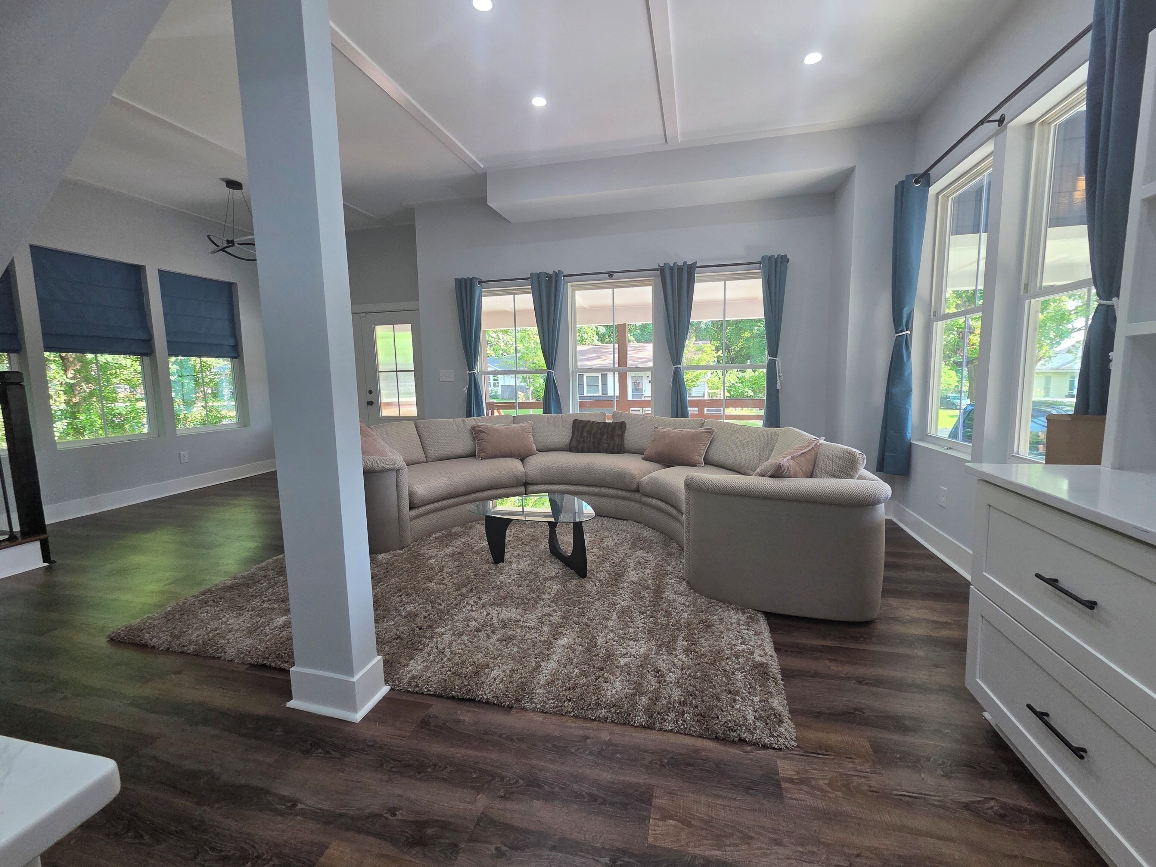A spacious living room with a large sectional sofa, a glass coffee table, and a view of the outdoors through large windows.