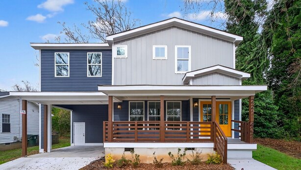 Ein zweistöckiges Haus mit überdachter Veranda, Garage und Garten mit Mulch und Pflanzen.