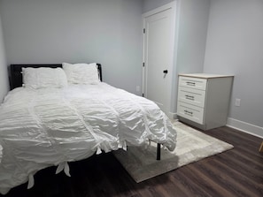 A bedroom with a bed, a nightstand, a dresser, and a door.