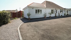 A single-story building with a tiled roof, a gravel driveway, and potted plants along the front. - Beachway (Holywell)
