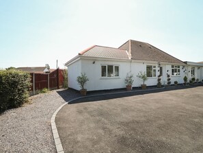 A single-story building with a tiled roof, a gravel driveway, and potted plants along the front. - Beachway (Holywell)