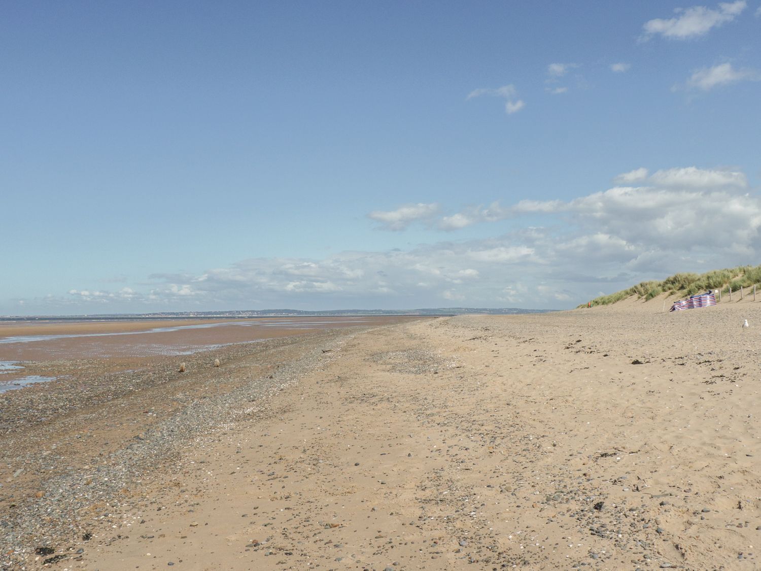 Une plage de galets et de sable, une dune et un drapeau sur la droite.