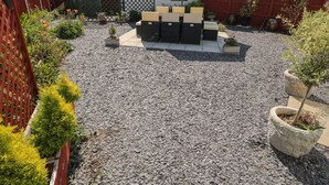 A backyard with a patio area, a small garden, and a house in the background. - Beachway (Holywell)