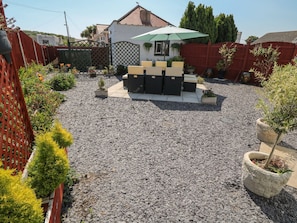 A backyard with a patio area, a small garden, and a house in the background. - Beachway (Holywell)