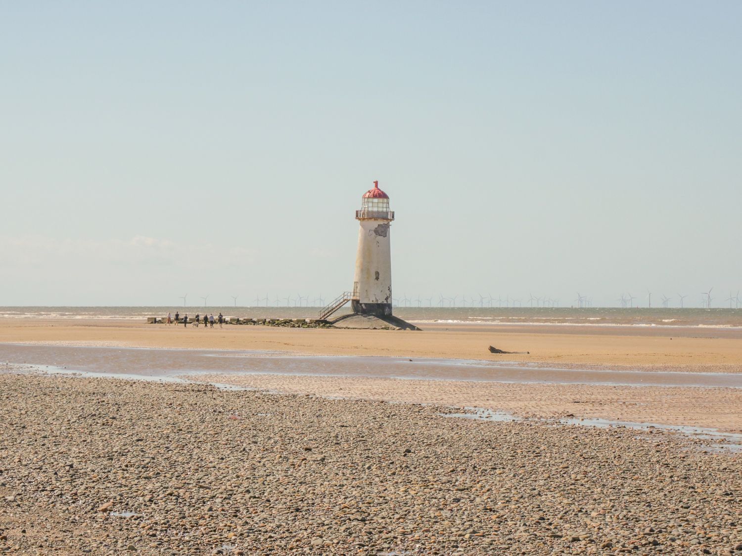 A lighthouse on a pebbly beach with a clear sky.