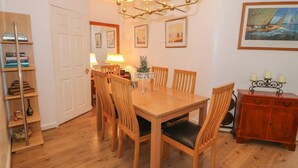 A dining area with a wooden table and chairs, a chandelier, and a bookshelf. - Beachway (Holywell)