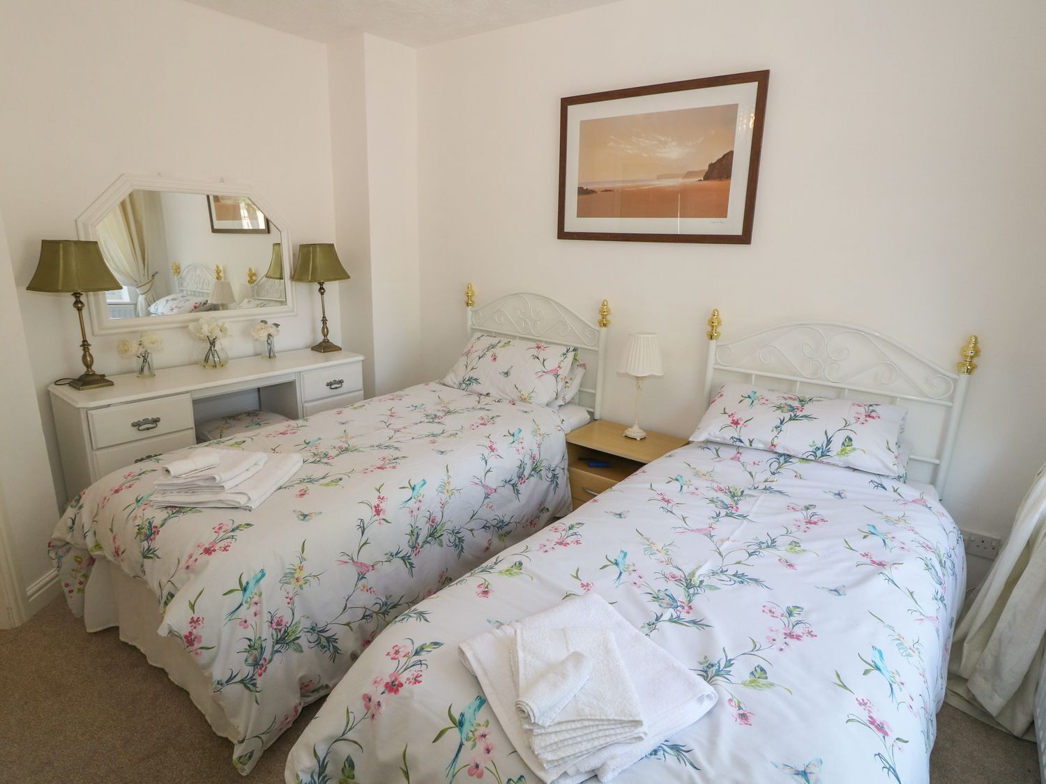 A twin bedroom with two beds, a dresser, a mirror, and a framed picture on the wall.