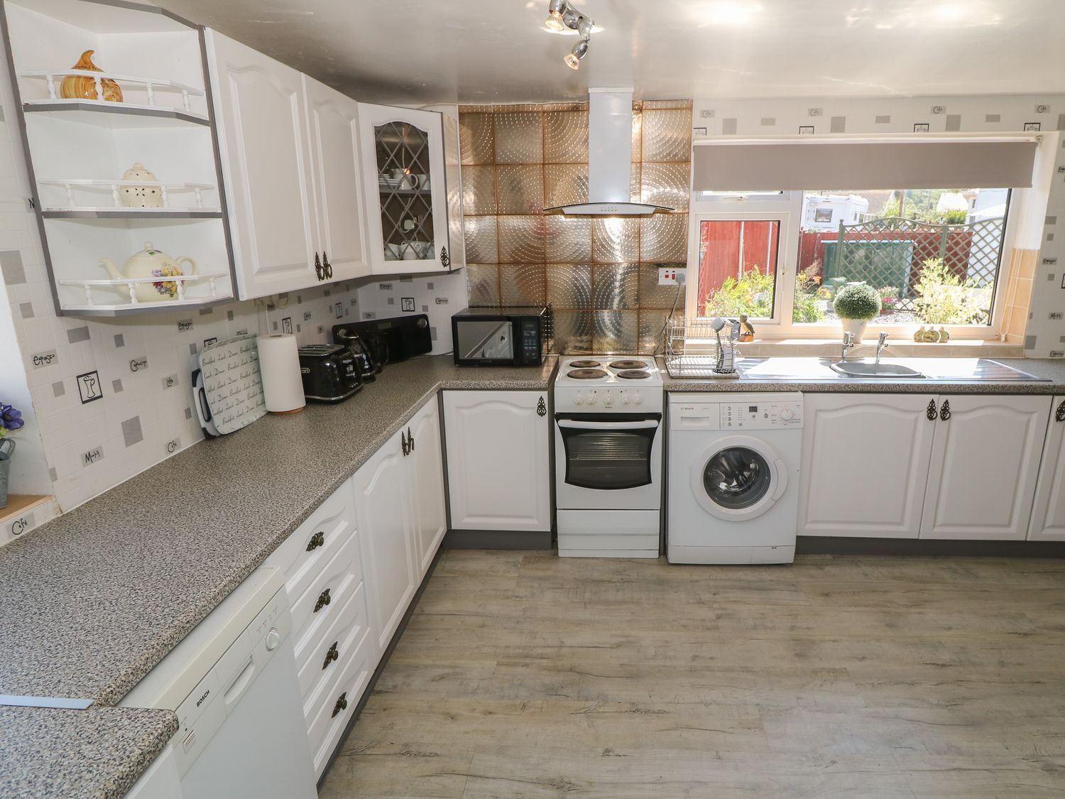 Una cocina compacta con armarios blancos, horno integrado, microondas y lavadora.