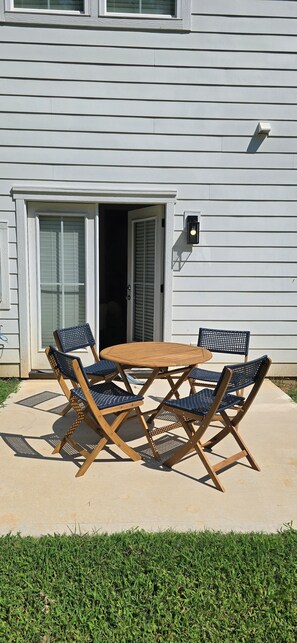 Eine Terrasse mit einem Holztisch und vier Stühlen, einer Glastür und einer wandmontierten Leuchte.