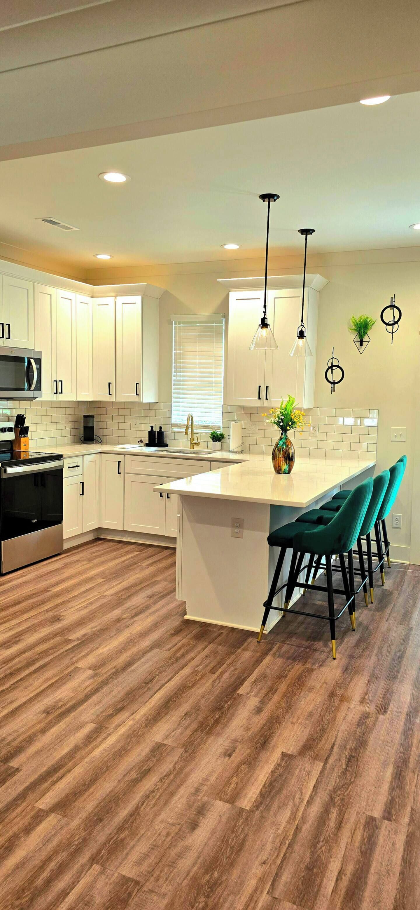 A modern kitchen with white cabinetry, a large island with bar stools, and wooden flooring.
