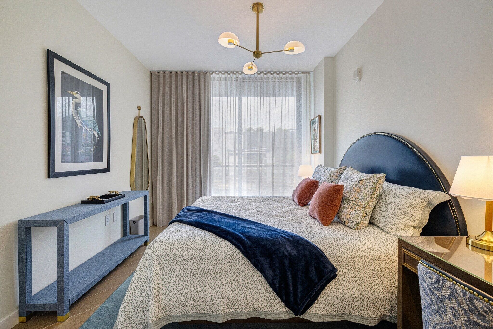 Une chambre d’hôtel avec un lit, une table de chevet, une lampe, des rideaux et un tableau encadré au mur.
