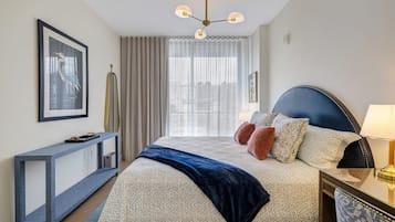 Une chambre d’hôtel avec un lit, une table de chevet, une lampe, des rideaux et un tableau encadré au mur.