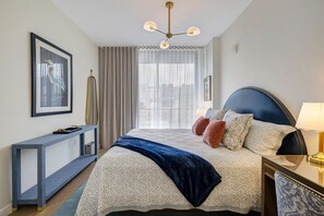 Quarto de hotel com cama, mesa de cabeceira, abajur, cortinas e um quadro na parede.