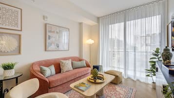 Un salon moderne avec un canapé, des fauteuils, une table basse et une grande fenêtre ornée de rideaux légers.