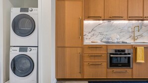 Una cocina con armarios de madera, horno Bosch, lavadora y encimera de mármol.