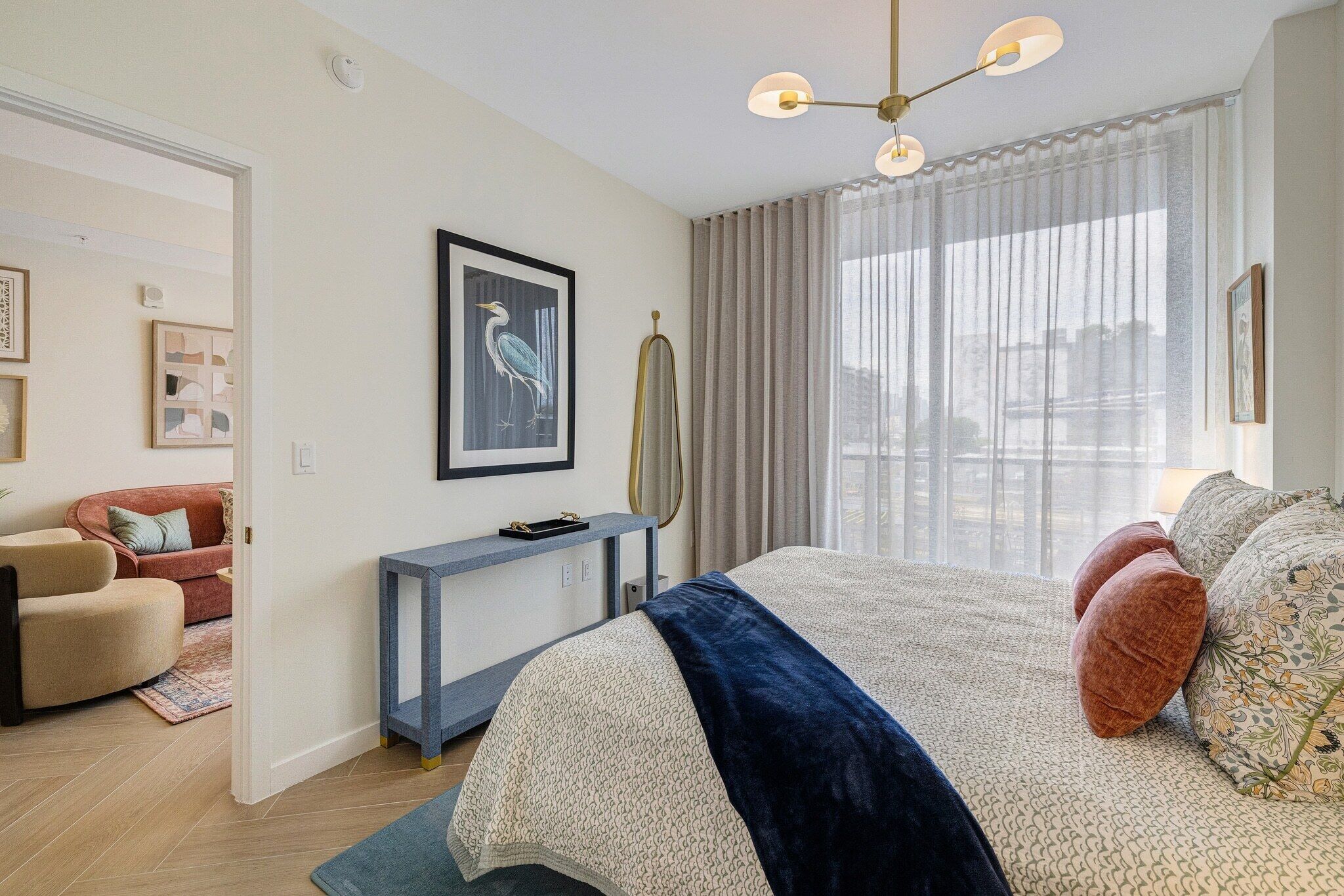Un dormitorio moderno con una cama grande, una consola, una obra de arte enmarcada y vistas por la ventana.