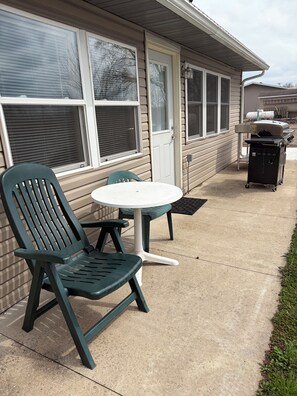 A patio with a green chair and a white table, a barbecue grill, and a house with beige siding and white trim. - River Front house with private boat slip, grill, canoe and more (Fountain City)