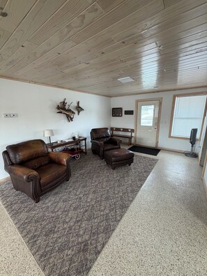 A room with a brown leather sofa, a matching ottoman, a wooden coffee table, and a wall-mounted deer head decoration. - River Front house with private boat slip, grill, canoe and more (Fountain City)
