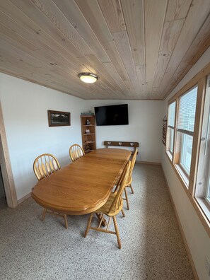 A room with a wooden dining table, chairs, a television mounted on the wall, and a window with blinds. - River Front house with private boat slip, grill, canoe and more (Fountain City)