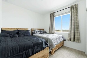 Ein Schlafzimmer mit zwei hölzernen Betten, einem Fenster mit Vorhängen und Blick ins Freie.
