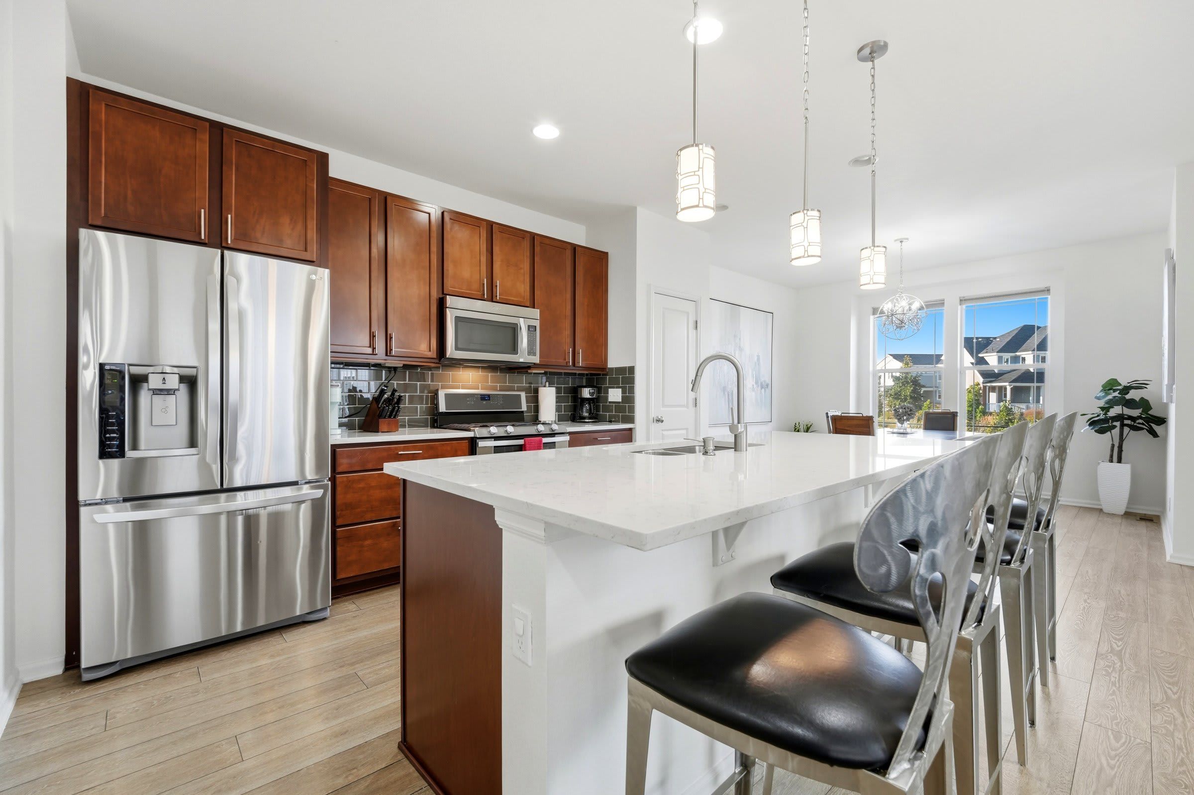 A modern kitchen with stainless steel appliances, wooden cabinets, a large island with bar stools, and pendant lighting.