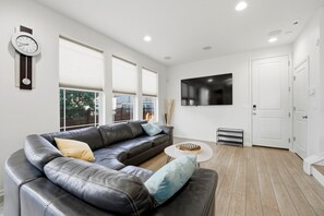 A modern living room with a leather sofa, a coffee table, and a flat-screen TV mounted on the wall. - Central Park Denver 3BR and Loft Near Anschutz  DIA (Denver)